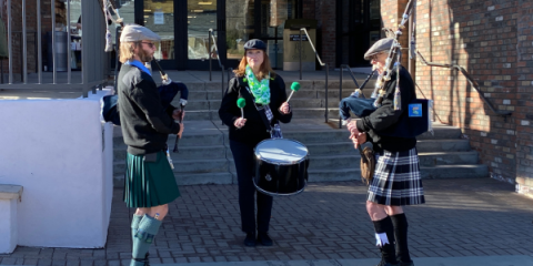 Two men with bagpipes flank woman playing drum